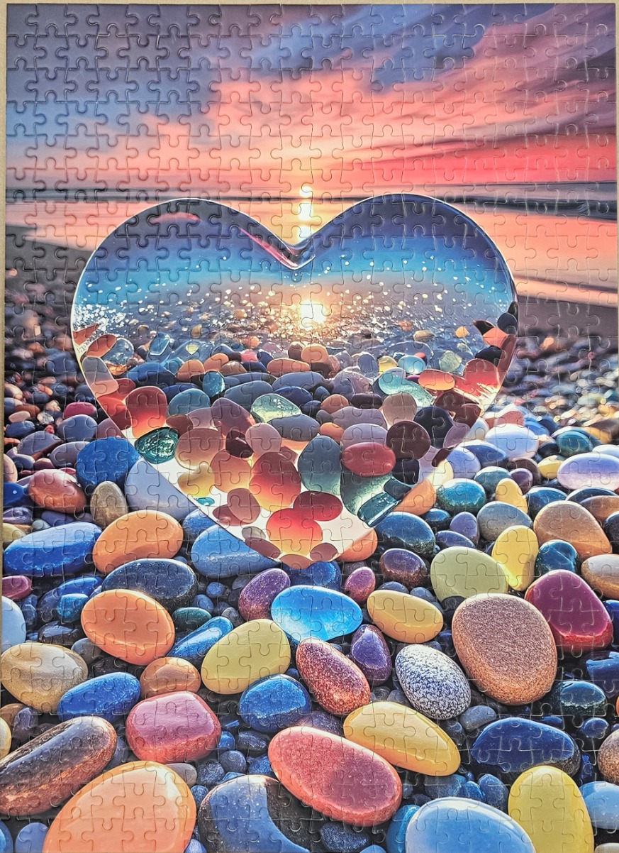 A heart-shaped window revealing a sunset over a pebble beach, set against a background of colourful stones.