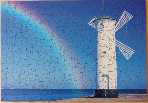 A lighthouse shaped like a windmill stands against a deep blue sky with a vibrant rainbow.