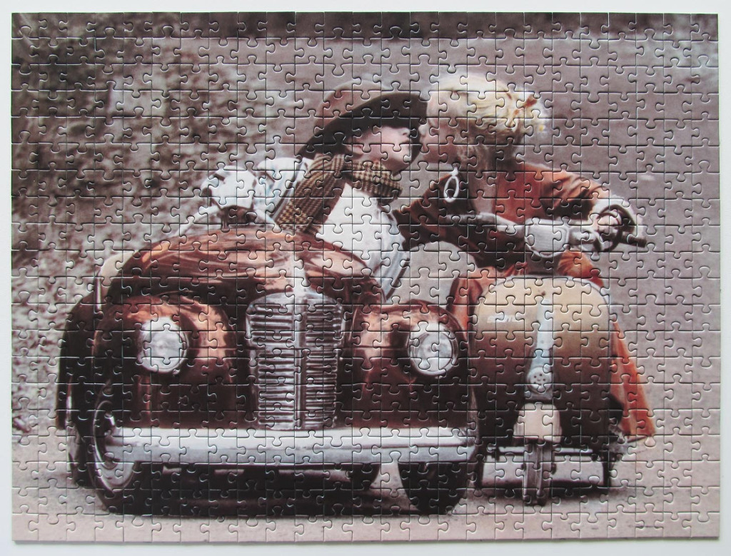 A vintage-style photograph of a young boy in a toy car and a girl on a scooter sharing a kiss.