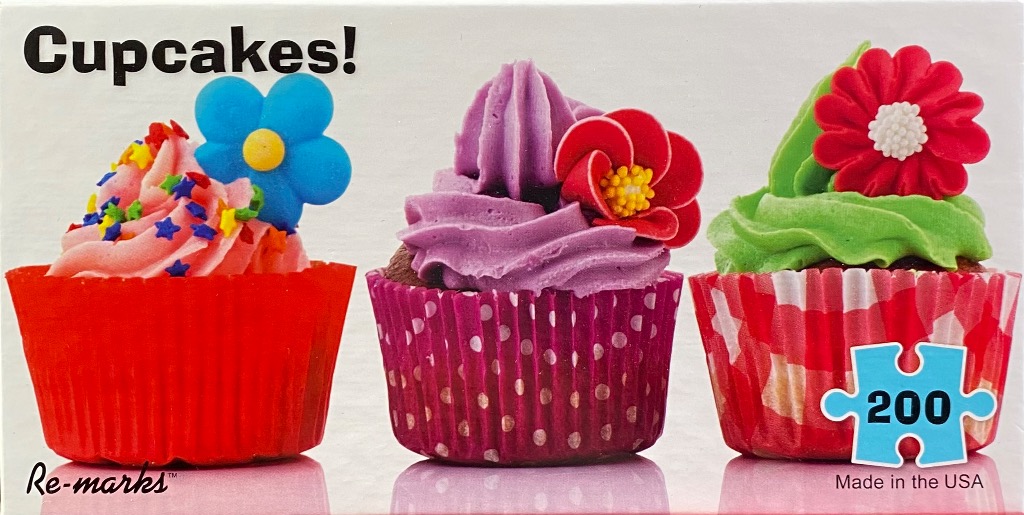 Three decorative cupcakes in patterned liners, each topped with vibrant frosting and a floral-shaped candy.