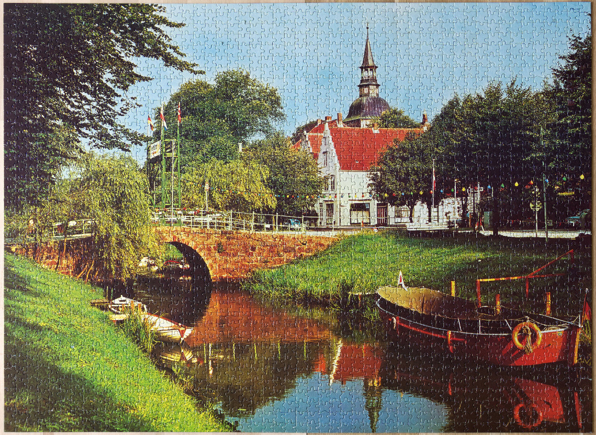 A peaceful canal scene with a stone bridge, red-roofed buildings, and a boat reflecting in the calm water.