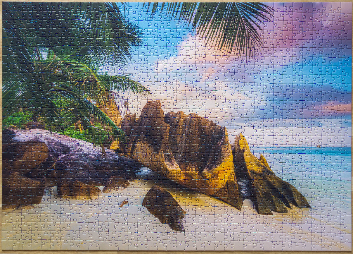Tropical beach scene with weathered granite boulders under palm fronds at sunset.