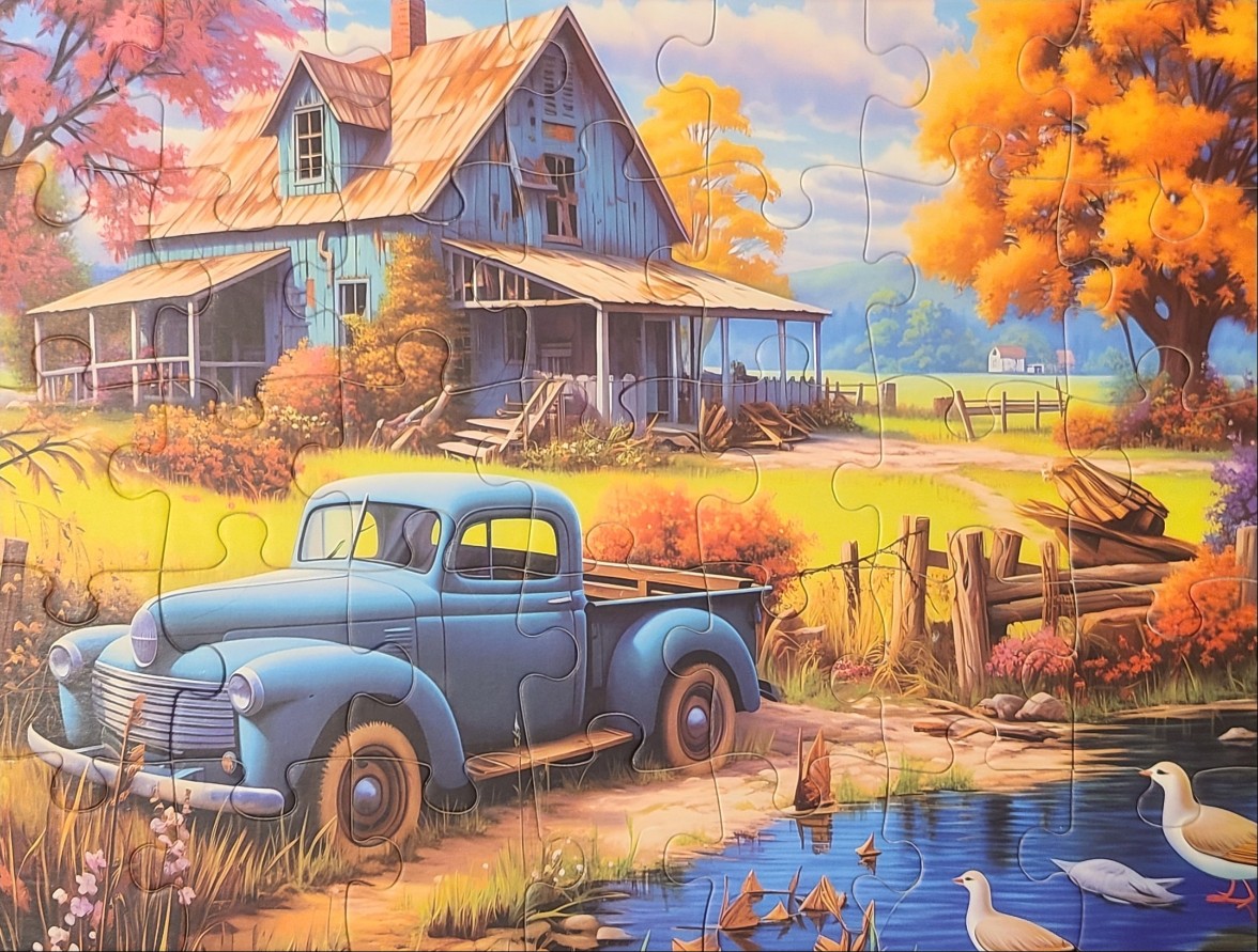 A blue vintage pickup truck parked in front of a blue farmhouse during autumn.