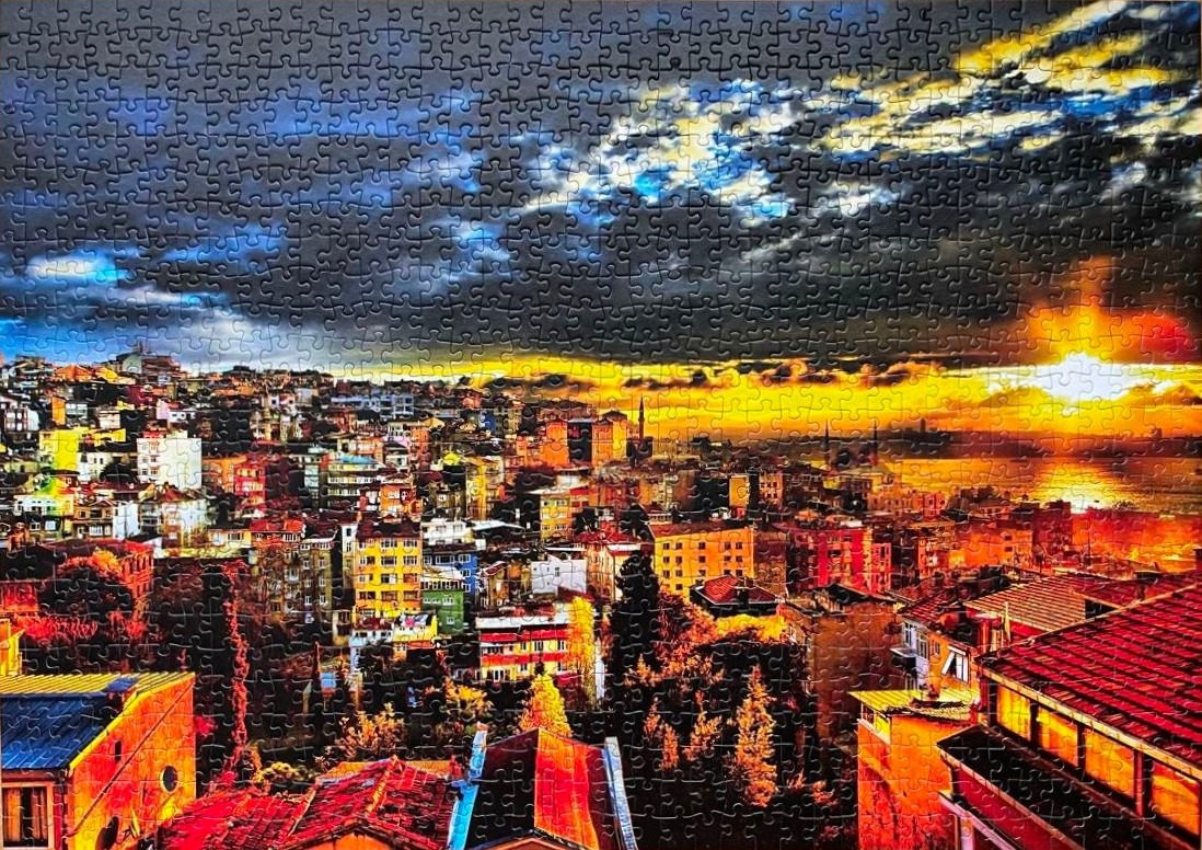 A panoramic sunset view over a densely packed Mediterranean-style hillside city with orange, red, and dark blue tones.