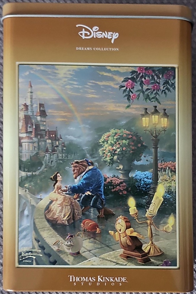 Belle and the Beast dance on a stone balcony with enchanted household objects, a castle, and rainbow in the background.