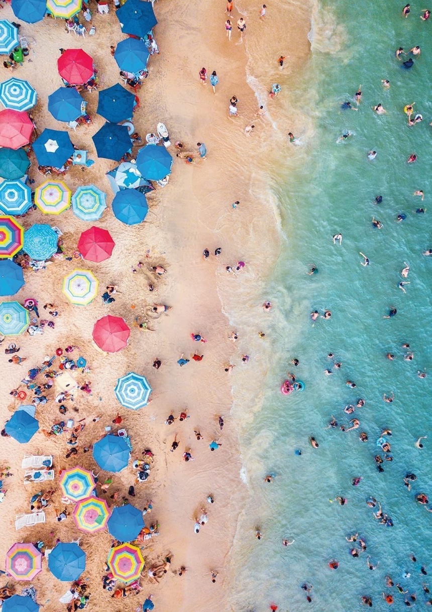 High-angle aerial view of a crowded beach with colorful umbrellas and people swimming in turquoise water.