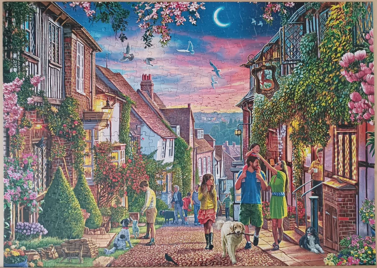 A charming English village street at twilight with people, dogs, and blooming flowers.