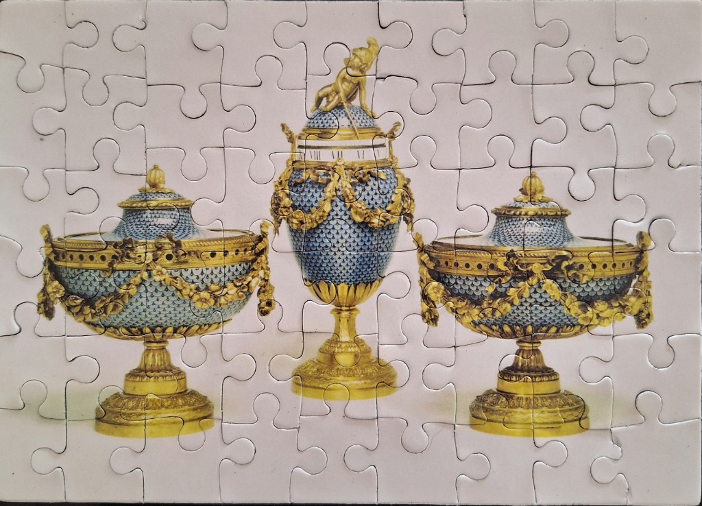 Three ornate, antique Sevres-style porcelain and gold urns against a light background.