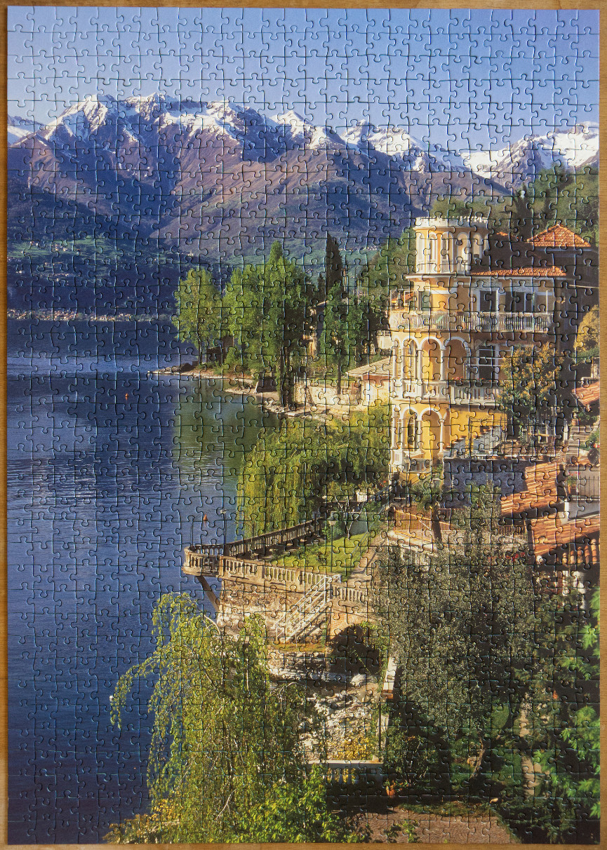 A sunny villa overlooking a deep blue lake with snow-capped mountains in the background.