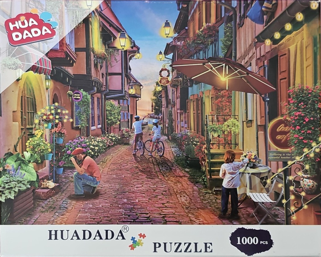 A street scene with European-style timber buildings, cyclists, and a photographer on a cobblestone road.