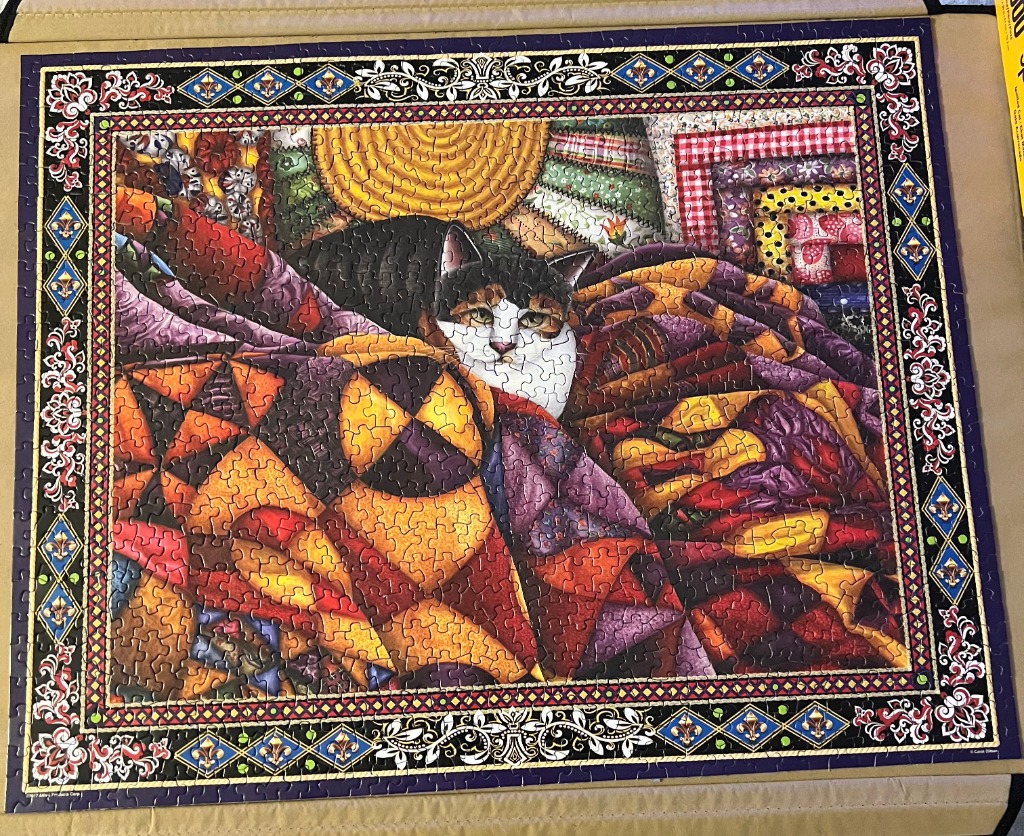 A black, white, and brown calico cat peeking out from underneath a vibrant, multi-coloured patchwork quilt.