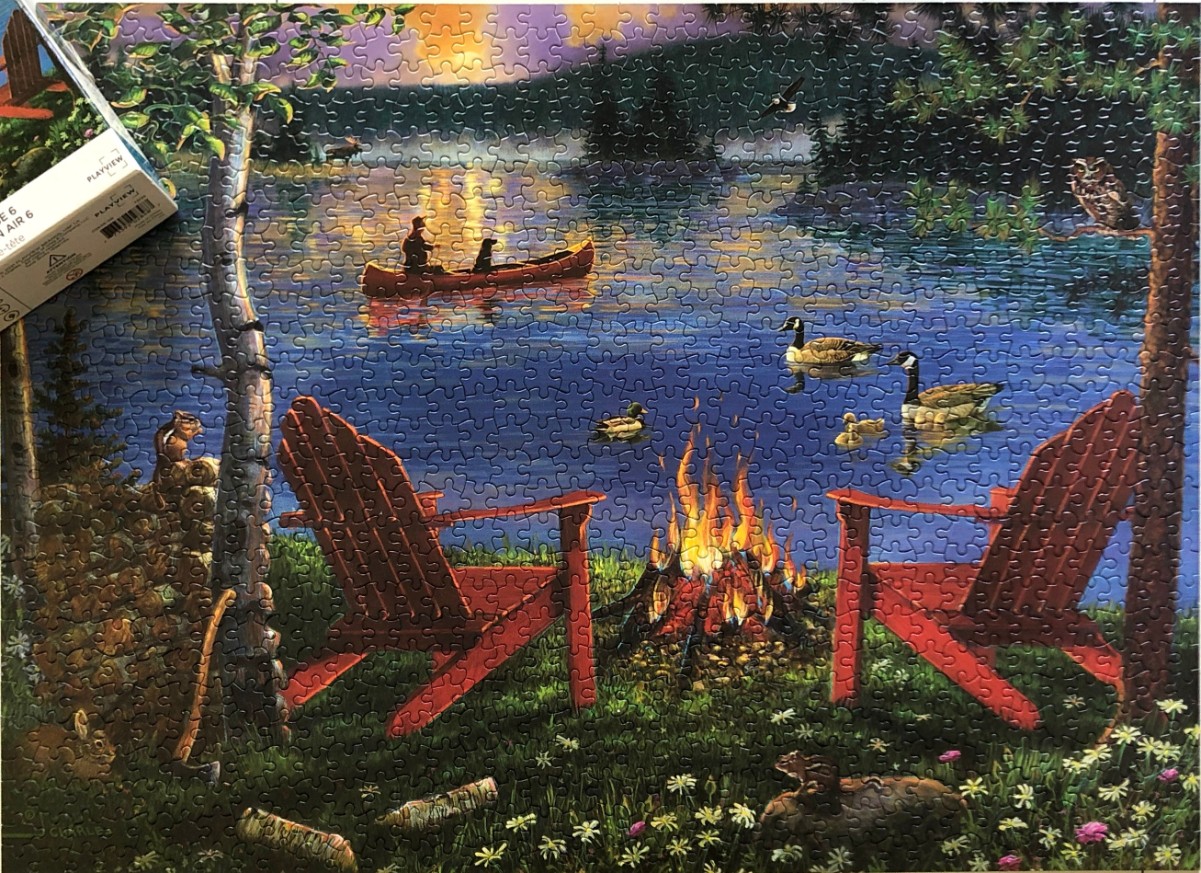 A peaceful lakeside scene at sunset with a campfire, two chairs, and a canoe on the water.