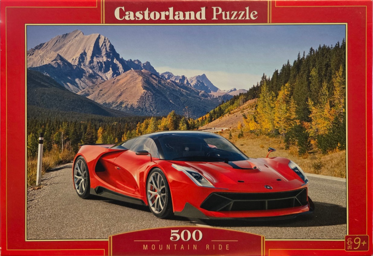 A red sports car parked on an asphalt mountain road with a range of rocky mountains in the background.