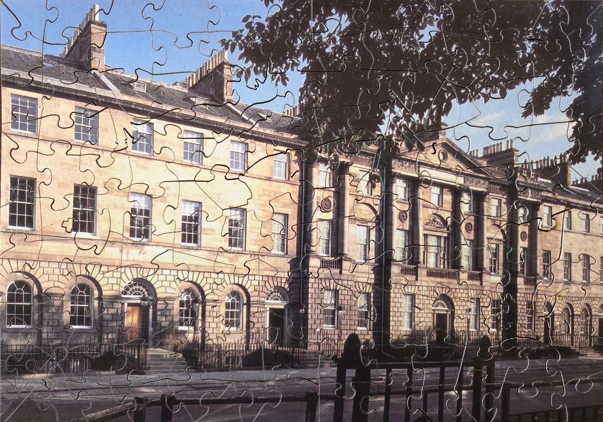 A stately stone Georgian terrace in Edinburgh with tall windows and arched doorways under a bright blue sky.