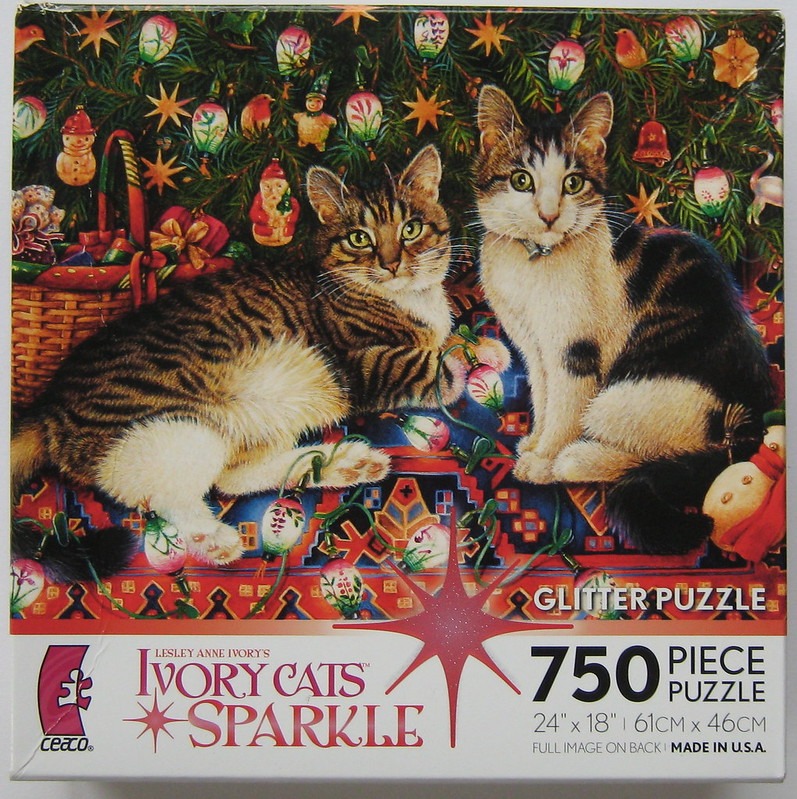 Two cats sitting in front of a decorated Christmas tree with ornaments and string lights.
