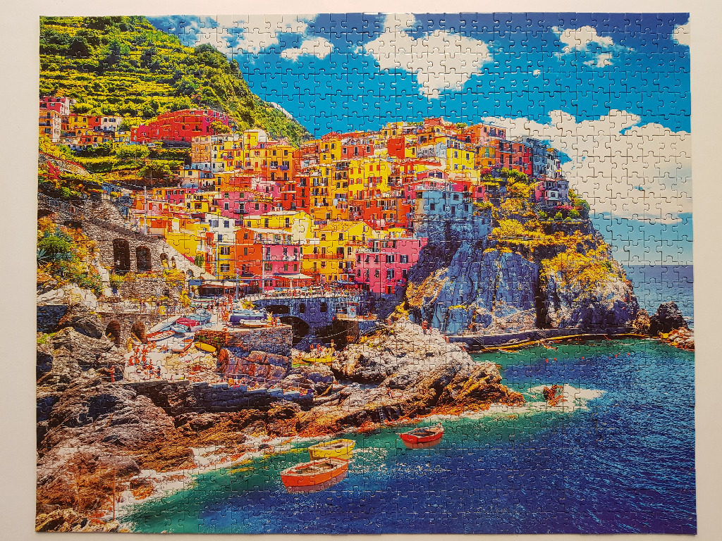 A vibrant, sunlit view of the coastal village of Manarola in Italy, featuring colorful houses on a rocky cliff by the sea.