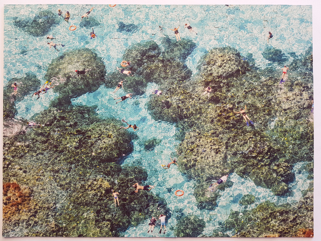 Aerial view of many people snorkeling and swimming over a vibrant coral reef in clear turquoise water.