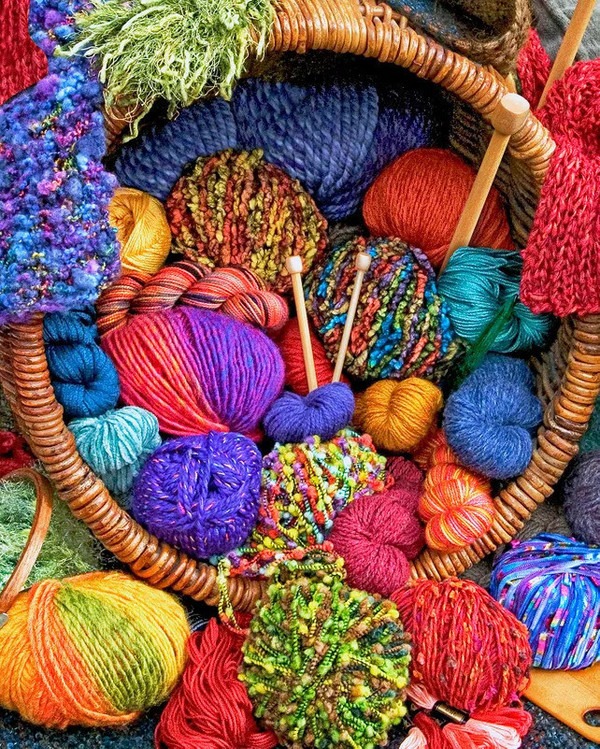 A woven basket overflowing with vibrant, multicolored skeins and balls of yarn.