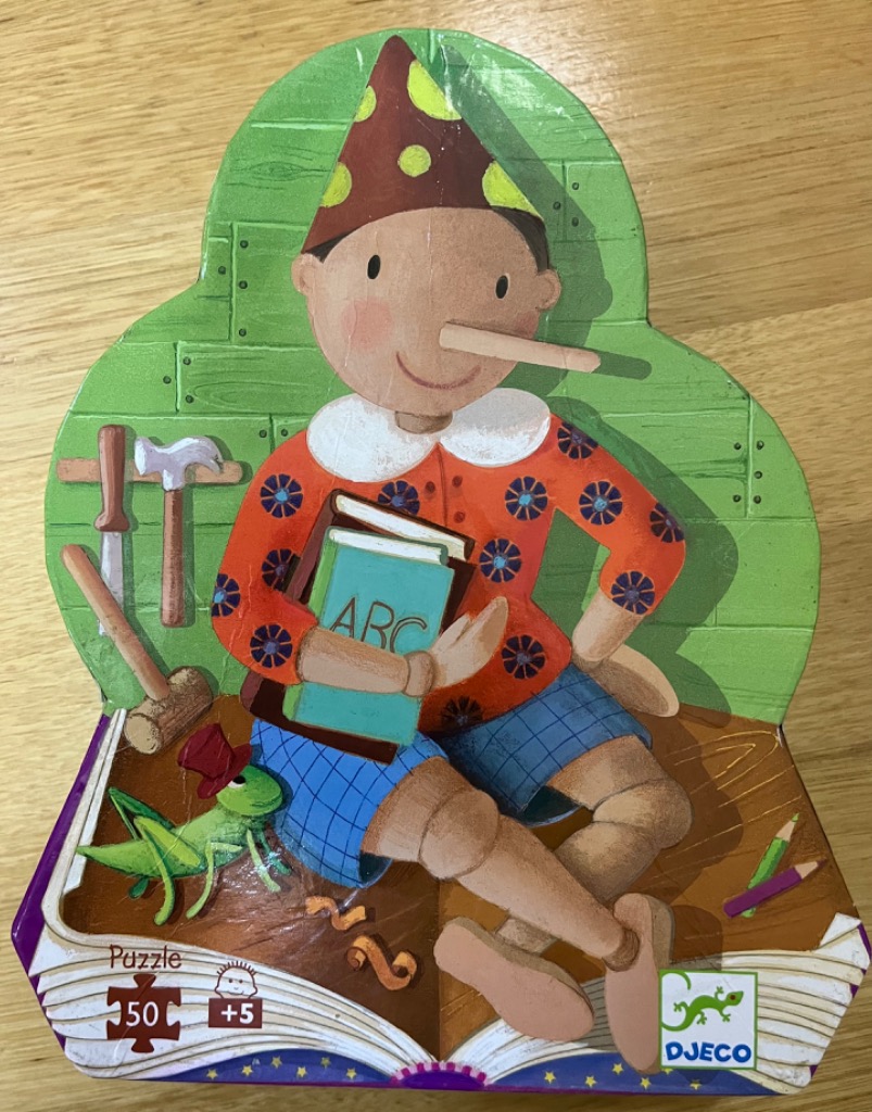 A whimsical illustration of Pinocchio holding an ABC book, accompanied by a cricket, set against a green wooden wall.