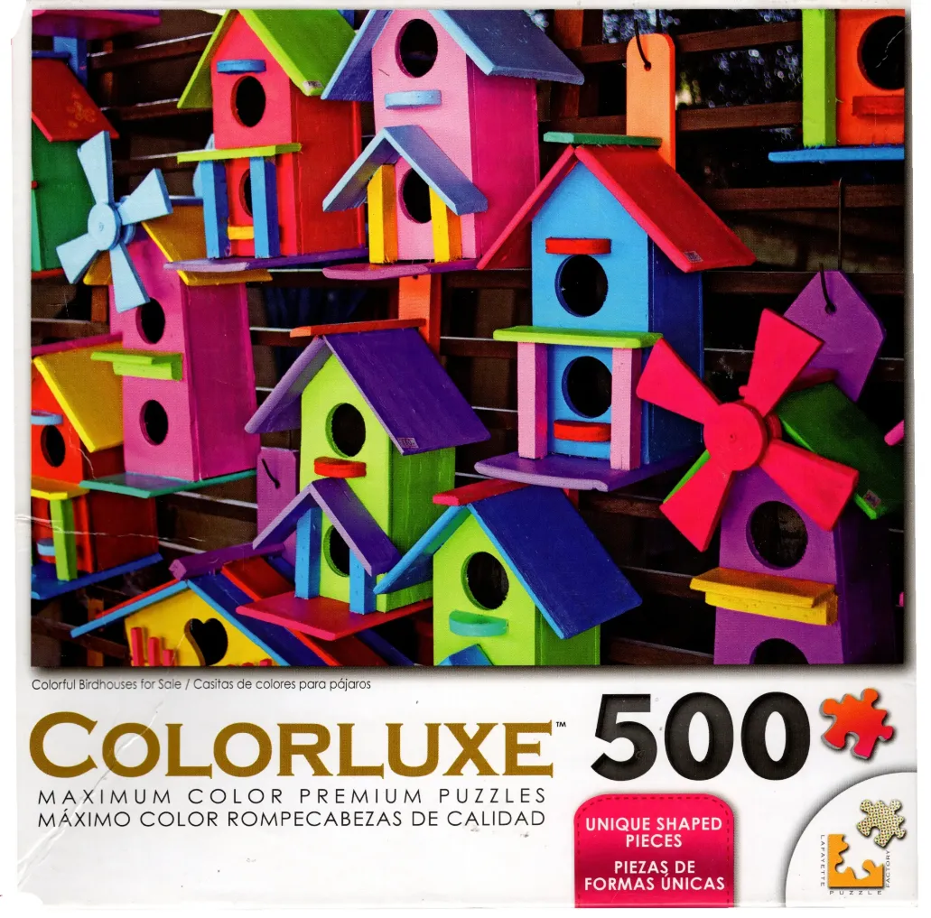 A collection of brightly painted wooden birdhouses hanging on a dark wood lattice fence.