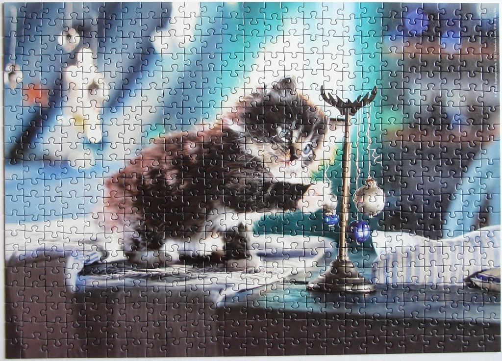 A fluffy black and white kitten playing with hanging Christmas ornaments on a stand.