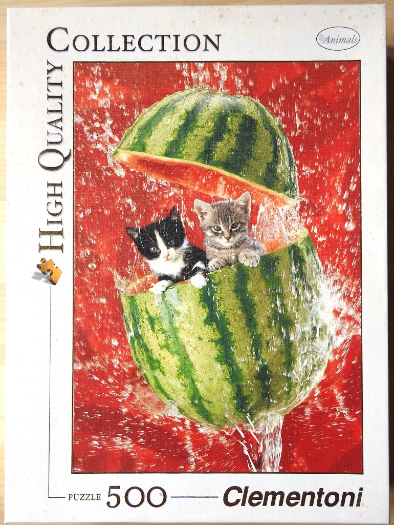 Two kittens peering out from inside a halved, dripping watermelon against a bright red background.