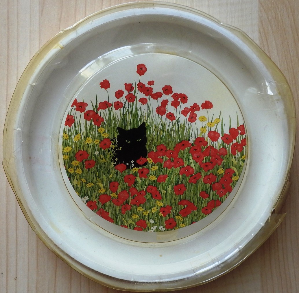 A black cat sitting in a field of bright red poppies and yellow wildflowers.