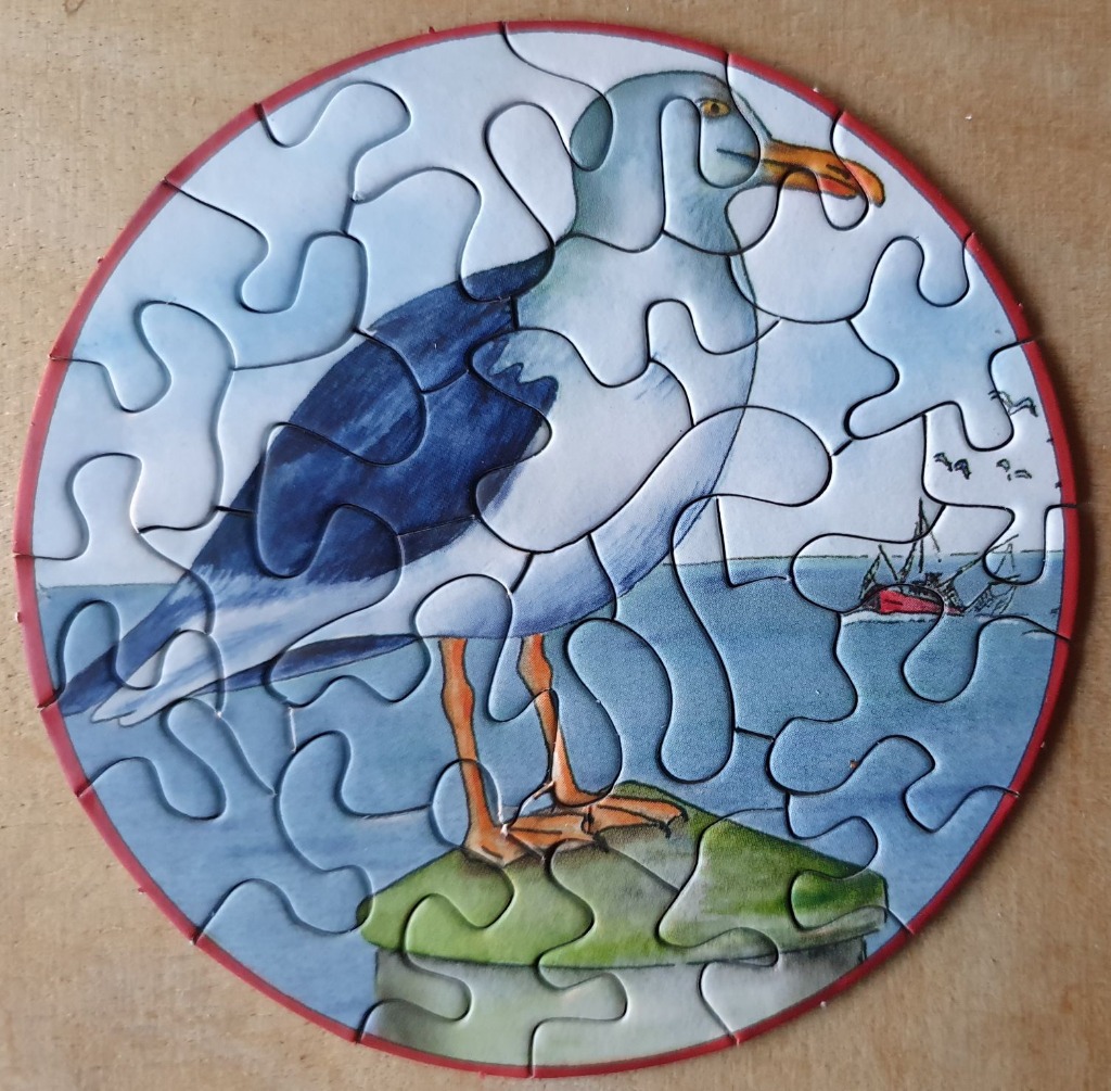 A circular illustration of a seagull standing on a green piling with a boat in the background.