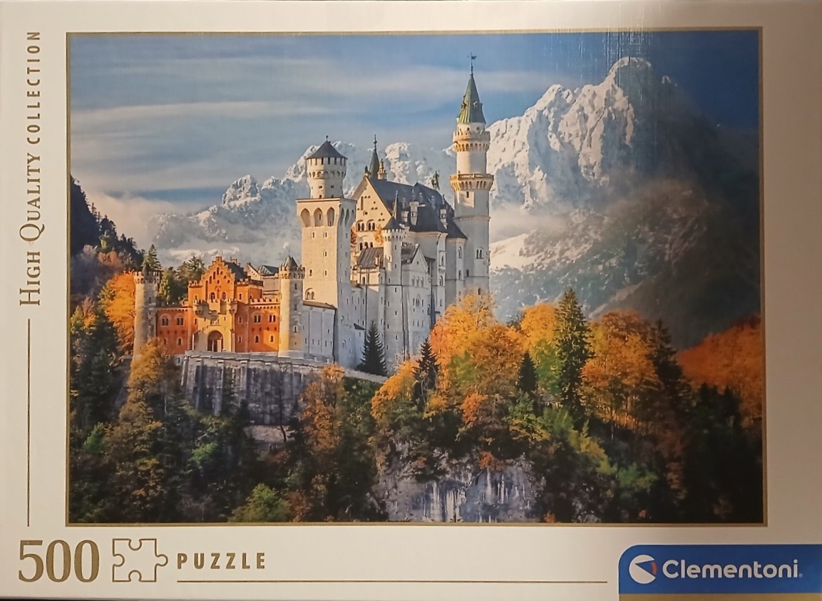 Neuschwanstein Castle perched on a mountain ledge during autumn with snow-capped Alps in the background.