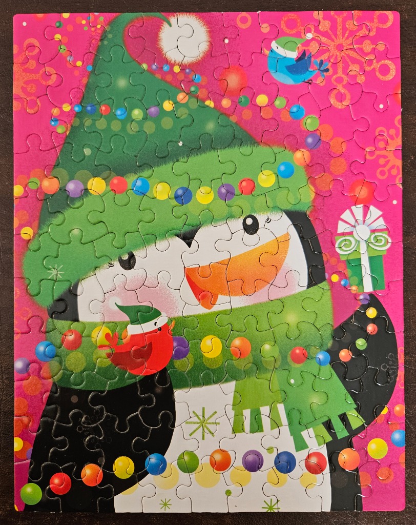 Two penguins wearing festive scarves and hats, decorated with Christmas lights on a bright pink background.