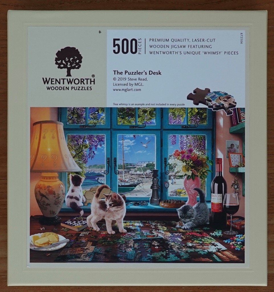 Three kittens playing on a table with a jigsaw puzzle in front of a window overlooking a seaside harbor.