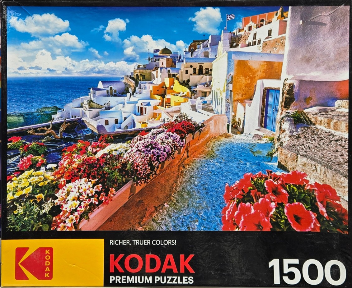 A scenic view of white buildings in Santorini, Greece, with vibrant flowers in the foreground overlooking the ocean.