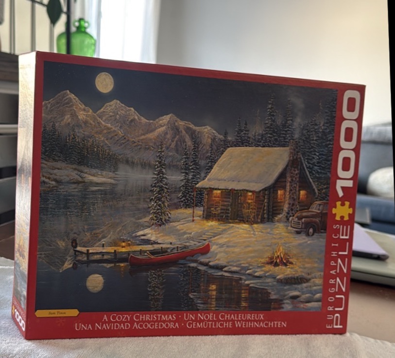 Winter cabin scene by a frozen lake with a canoe and mountains under a full moon.