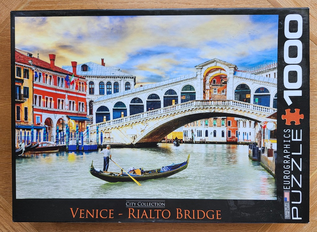 A gondolier rowing a gondola on a Venetian canal in front of the Rialto Bridge at sunset.
