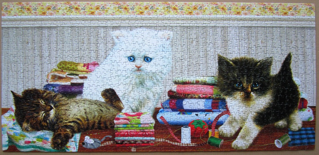 Three kittens sitting among stacks of colorful fabric and sewing supplies.