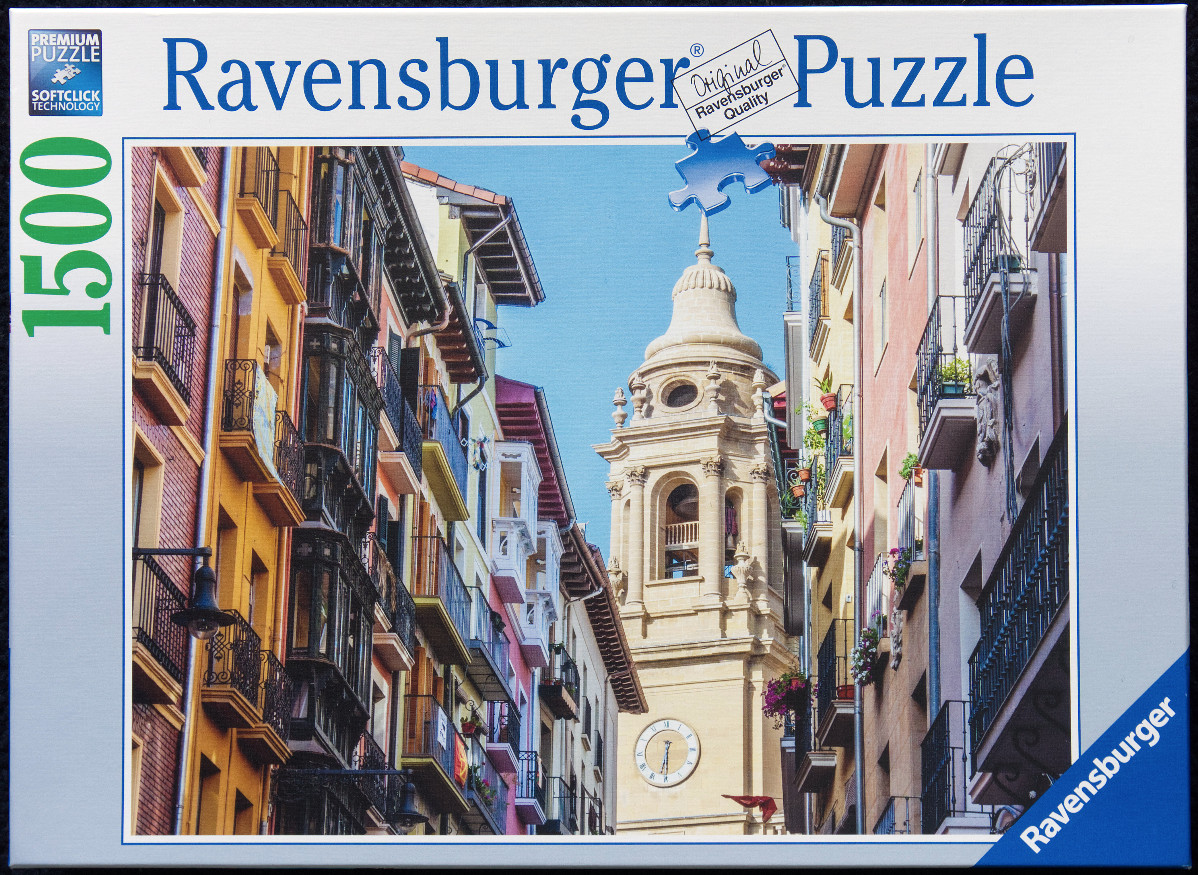 A view up a narrow European street toward a stone church bell tower with colorful buildings on either side.