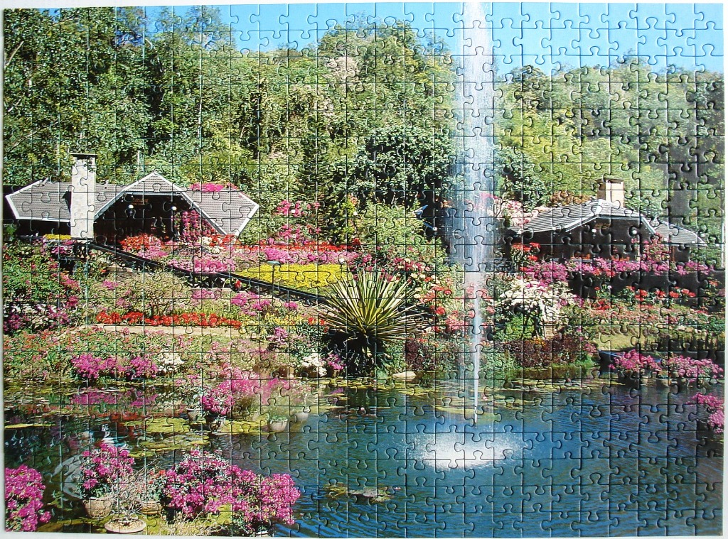 A peaceful garden scene featuring a tiered pond, a fountain, colorful flowers, and rustic cottages nestled in lush trees.