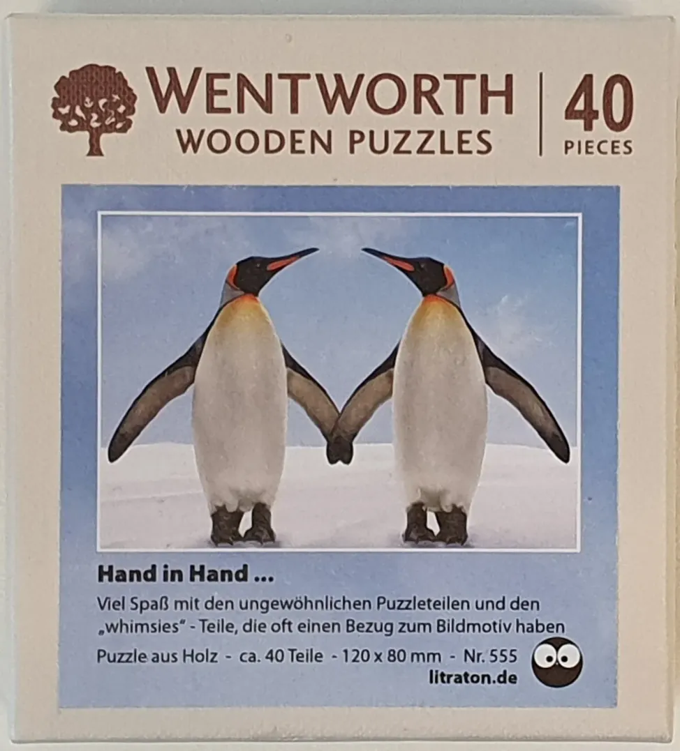 Two king penguins standing on snow and touching flippers as if holding hands against a light blue sky.