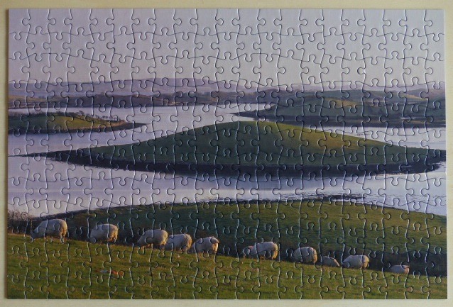 A scenic landscape of sheep grazing in a green hillside meadow overlooking a calm, reflective lake and rolling hills.