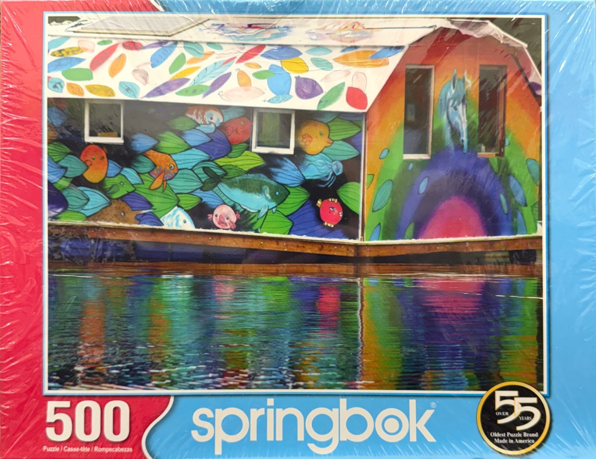 A brightly painted, mural-covered floating house on water reflected in the surface below.