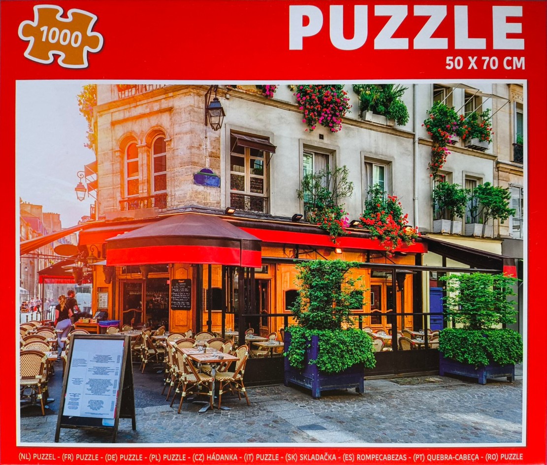 A charming Paris-style cafe terrace with outdoor seating and vibrant flower-filled balconies.