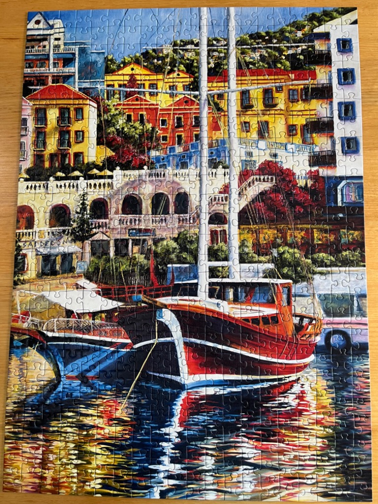 Oil painting of a red wooden boat moored in a sunlit Mediterranean harbor with colorful terraced buildings.