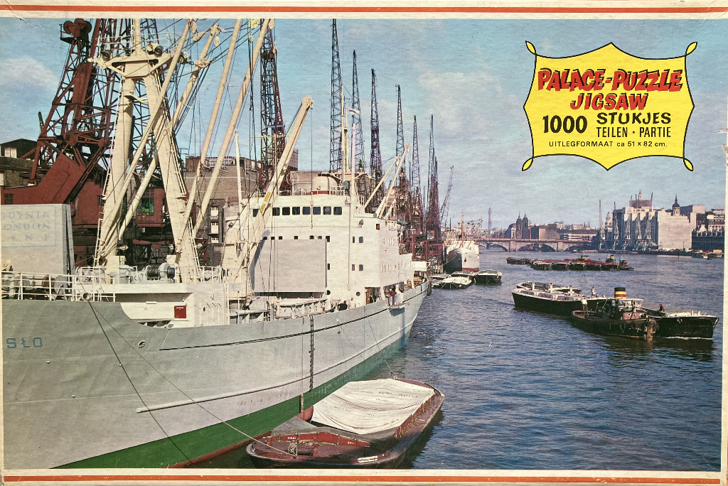A cargo ship docked in a busy industrial harbor with cranes and a river scene in the background.