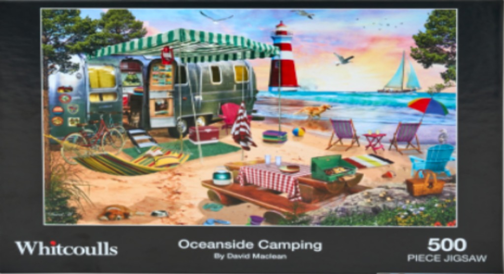 A sunny seaside campsite featuring a silver vintage trailer, a red and white lighthouse, and beach chairs on the sand.