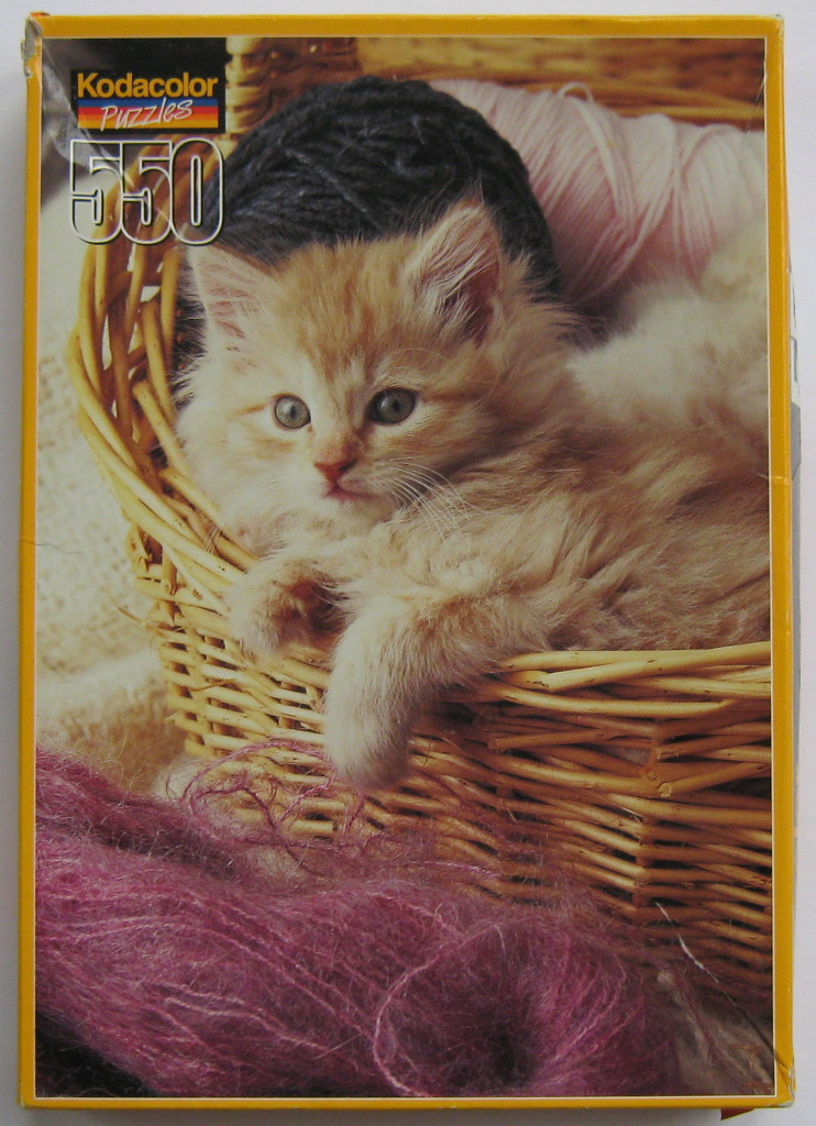 A fluffy ginger kitten sitting inside a light brown wicker basket filled with balls of yarn.