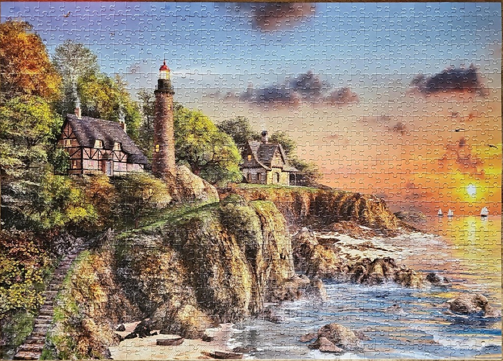 A lighthouse and cottages on a cliffside overlooking the ocean at sunset.