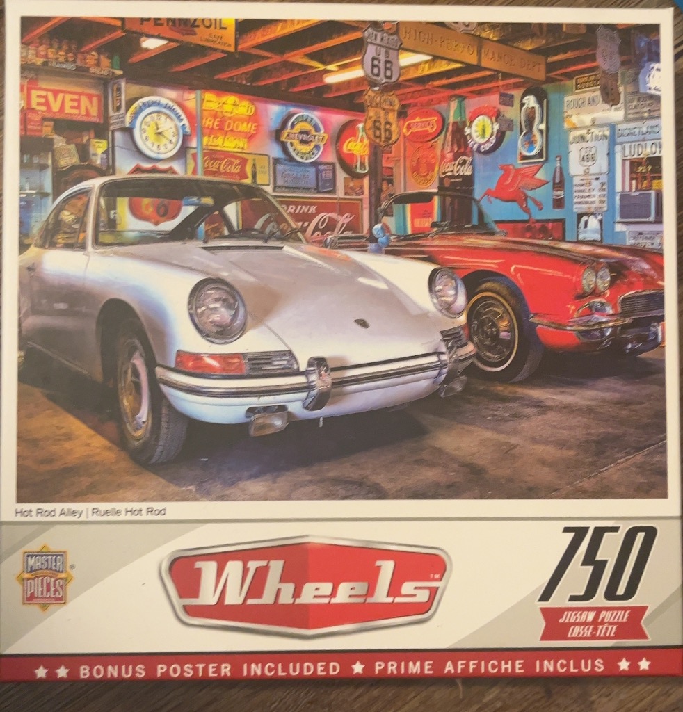 A silver vintage sports car and a red convertible parked inside a garage filled with automotive memorabilia and signs.