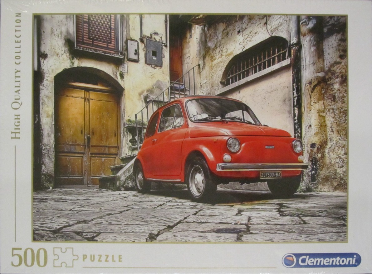 A vintage red Fiat 500 car parked on a cobblestone street in front of an old Italian building.