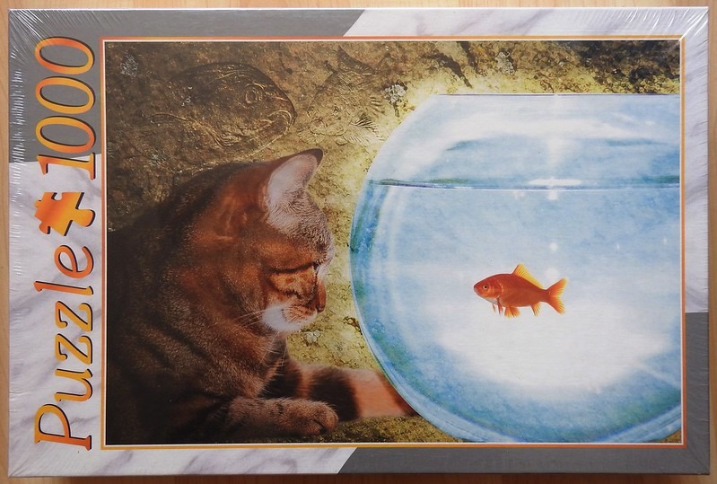 A brown tabby cat looking at a single goldfish in a spherical glass bowl against a textured rock-like background.