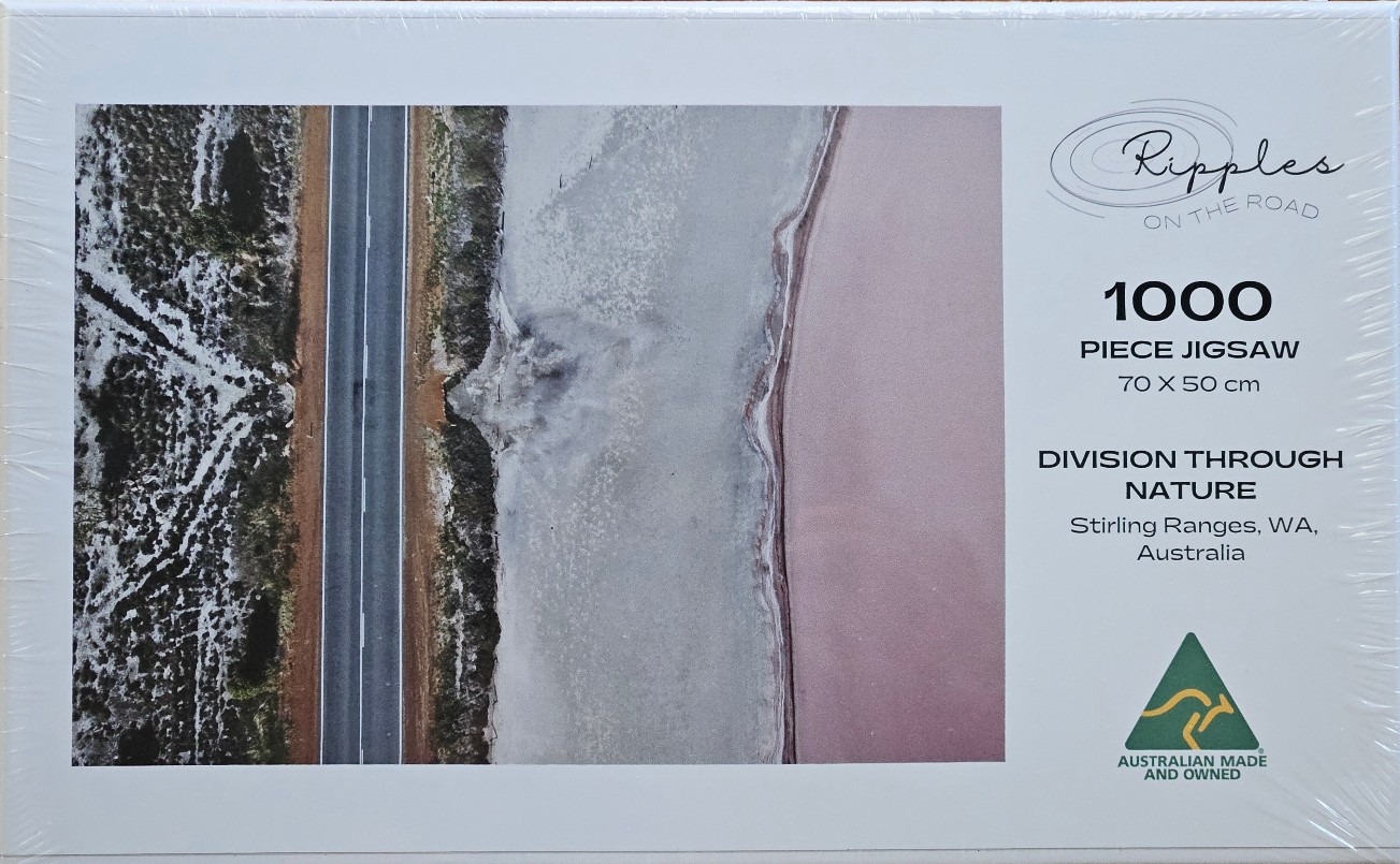 Aerial view of an asphalt road separating a dry, patterned landscape from a pink salt lake.